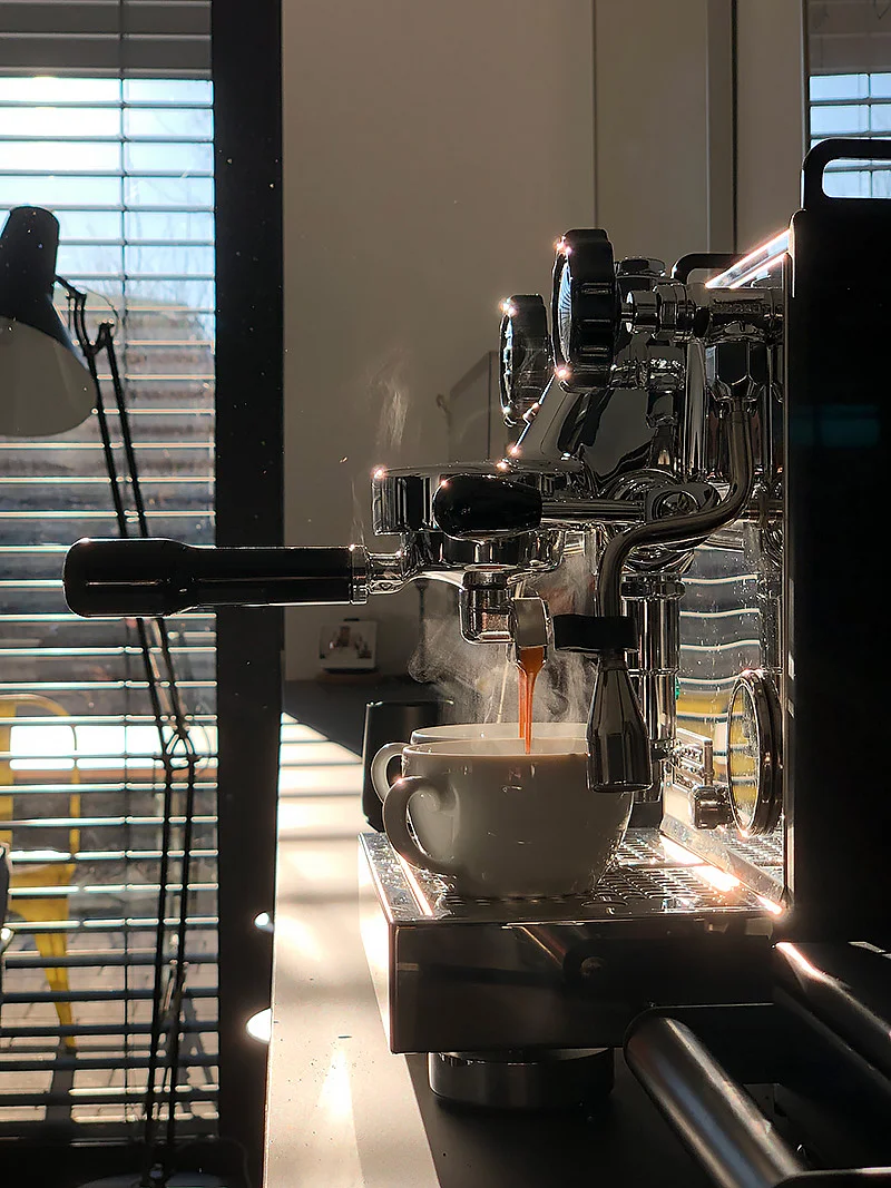 Espressomaschine mit einer Tasse, aus der frisch gebrühter Kaffee fließt, in einem hellen Raum.