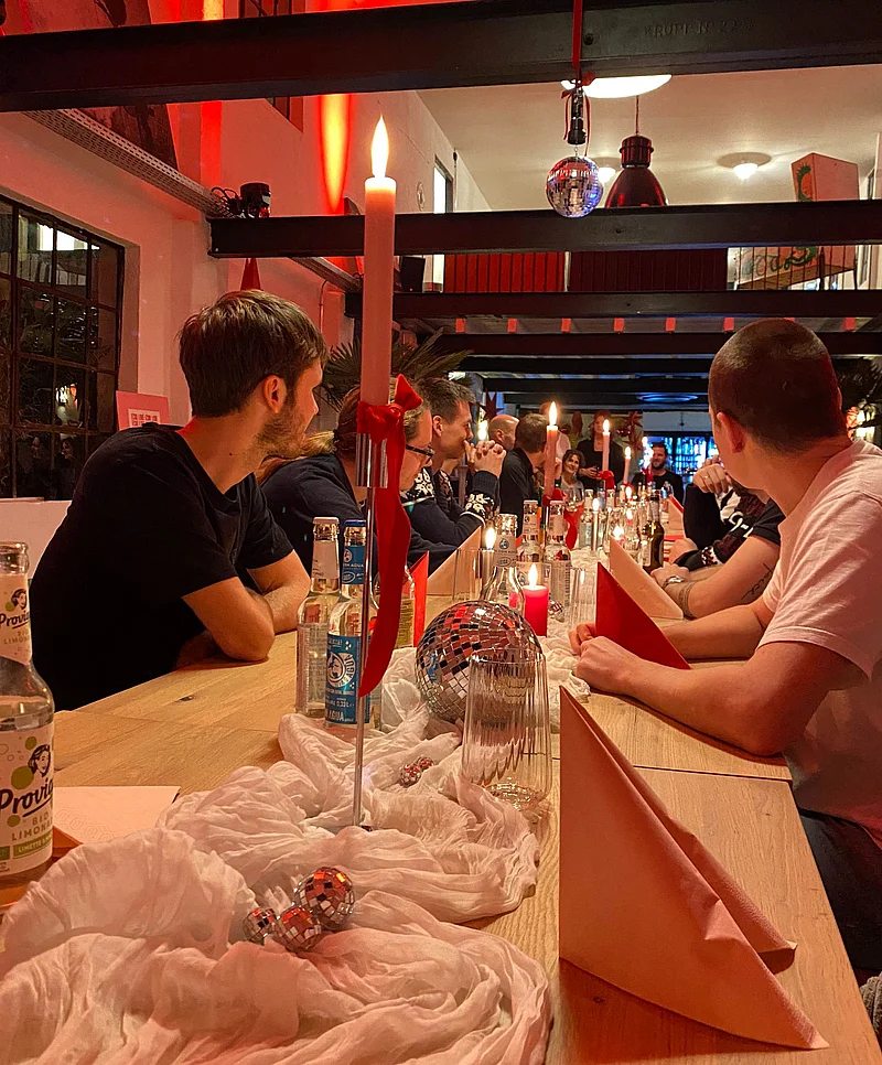 Esstisch mit Kerzen, Getränken, einer Discokugel, Dekorationen und Menschen, die an den Seiten sitzen.