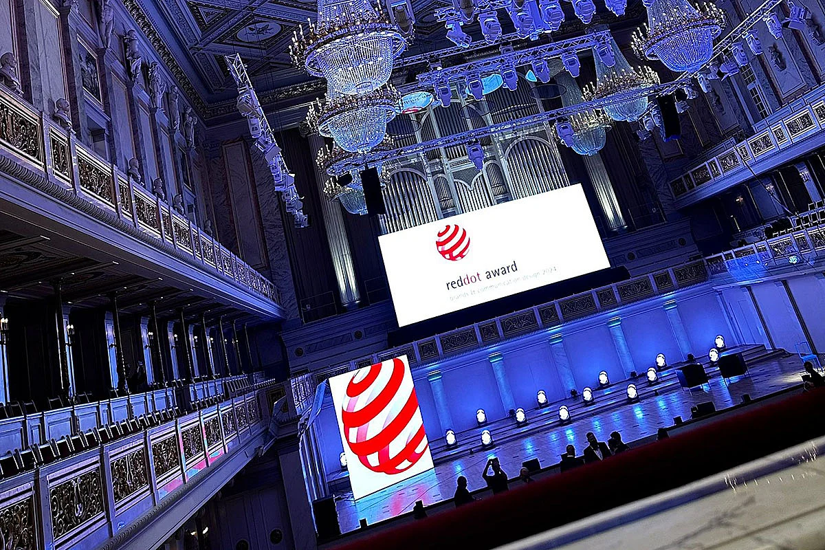 Ein eleganter Veranstaltungsort mit einem großen Bildschirm, der den Red Dot Award zeigt, und beleuchtetem Boden.