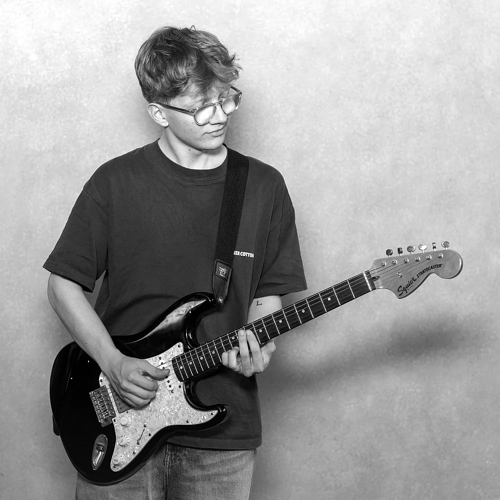 Junger Mensch mit Brille spielt E-Gitarre in Schwarz-Weiß.