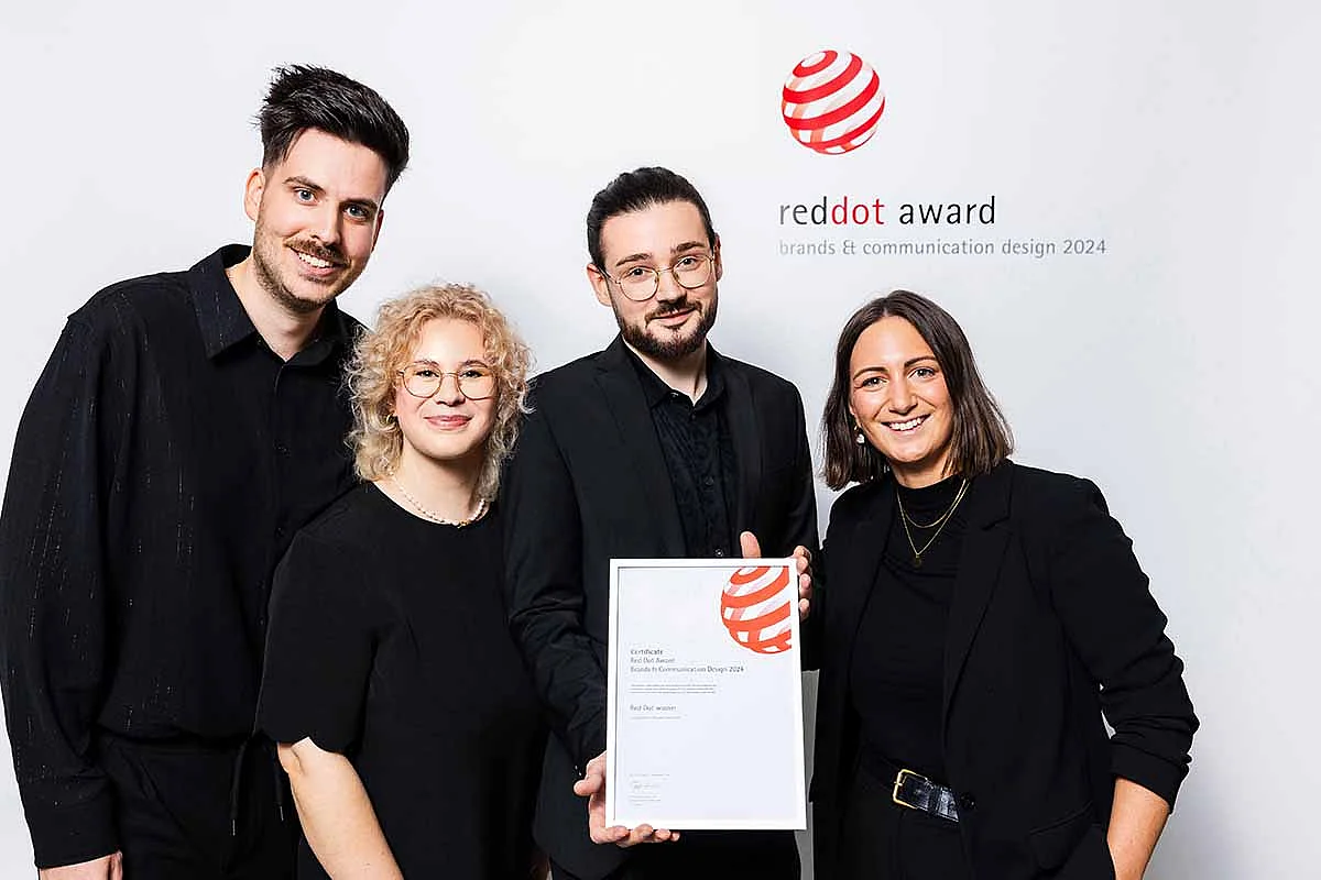 Vier Personen in schwarzer Kleidung halten eine Auszeichnung der Red Dot Awards vor einem weißen Hintergrund.