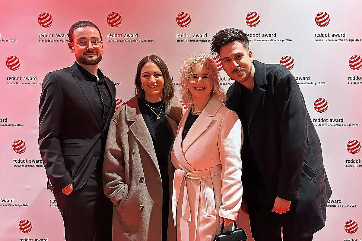 Vier Personen posieren vor einem roten Teppich mit Red Dot Award-Logos.