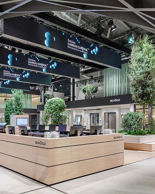 Moderne Ausstellungsfläche mit Bäumen, Computerarbeitsplätzen und großen Werbebannern.