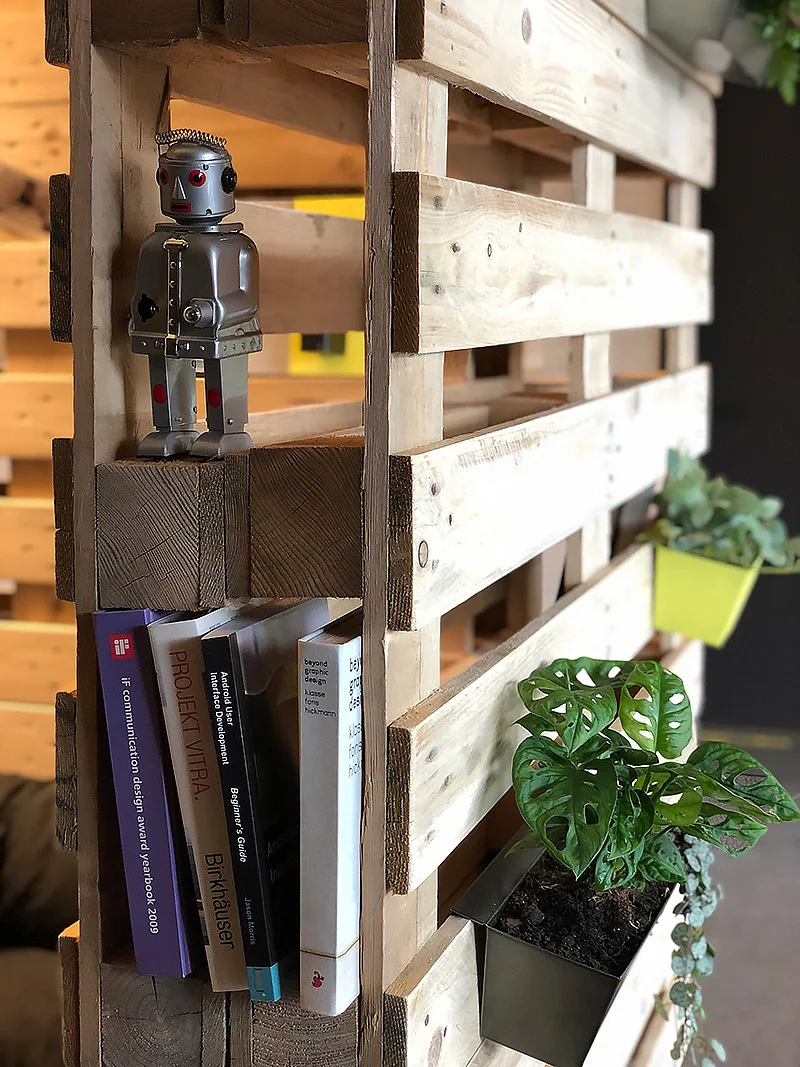 Ein Holzregal mit einem Spielzeugroboter, Büchern und Pflanzen.
